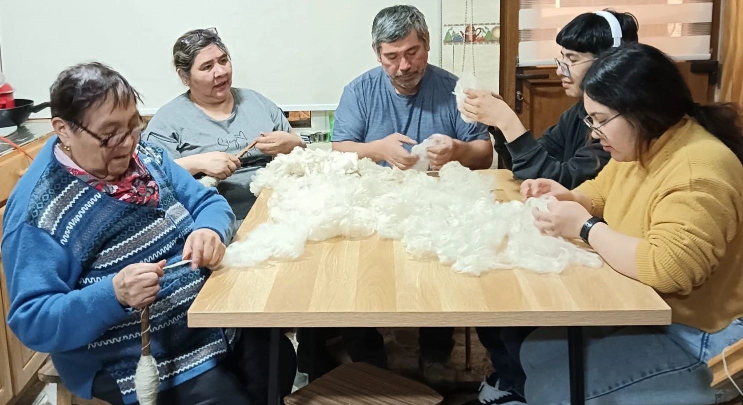 Personas escarmenando lana alrededor de una mesa